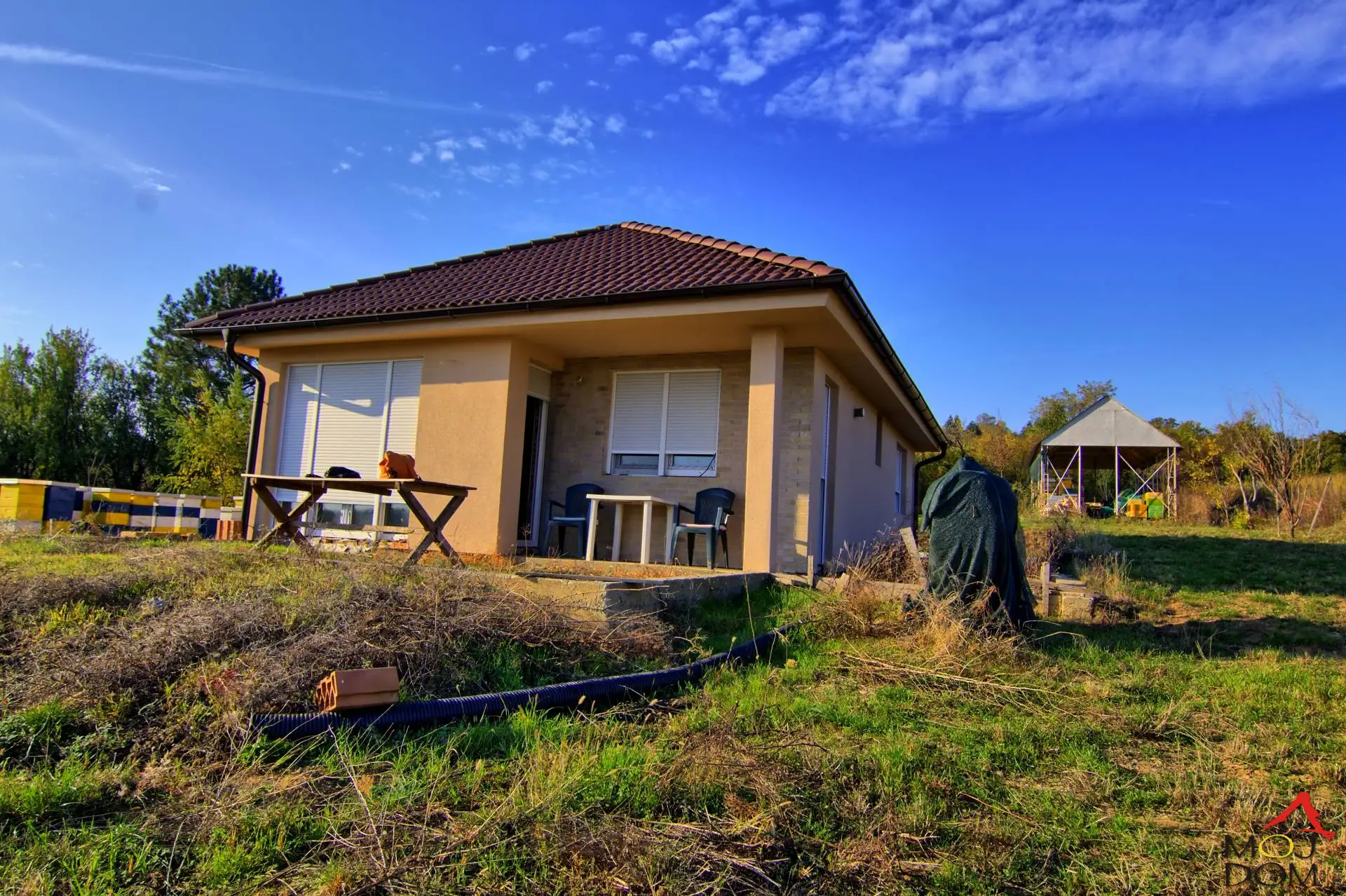We are selling a three-room weekend house of 74m² in the weekend zone of Hopovo settlement, on a spacious and flat plot of 2200m². The house is well-built and prepared for finishing works – painting and final repairs. It is located in a peaceful environment, in a c